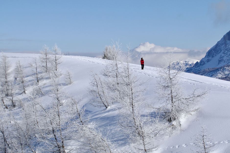 A person hiking across a snowy mountain ridge in Corvara, Italy during winter.