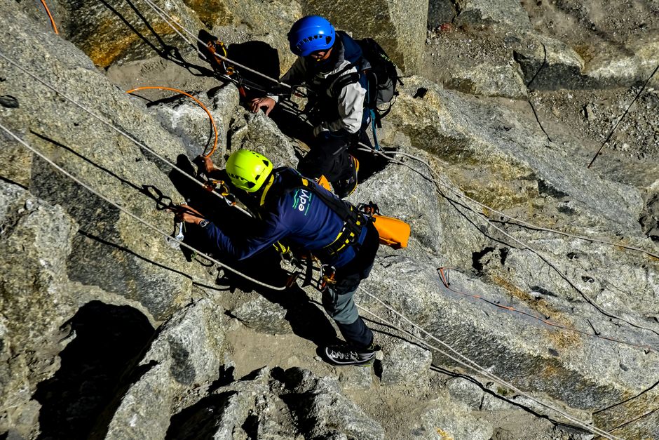 Two climbers scale a rocky mountain with ropes and safety gear, showcasing adventure and teamwork.